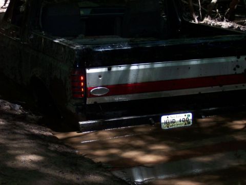 1996 Ford Bronco - A black pickup truck is stuck in mud, showing its rear end with a distinctive red and silver stripe on the tailgate.