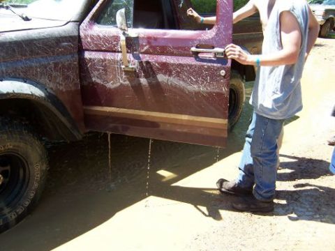 1996 Ford Bronco - A muddy 1996 Ford Bronco sits with its driver's door ajar, water pooling around its tires and dripping from its frame.