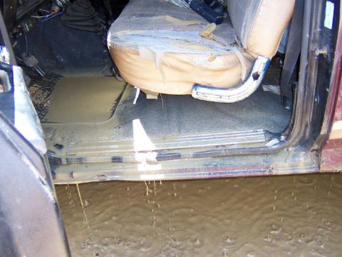 1996 Ford Bronco - Interior of a vehicle filled with mud and water, seats are torn.