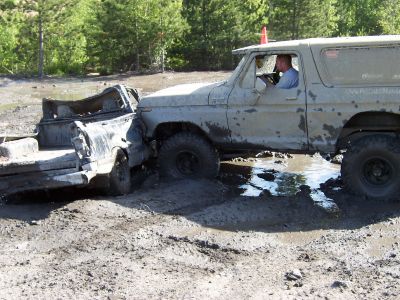 1996 Ford Bronco - A mud-splattered 1978 Ford Bronco is stuck in a muddy terrain, with its front bumper against a damaged truck bed.