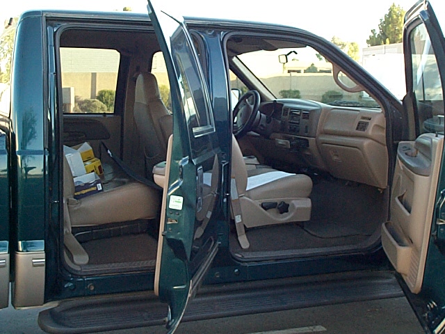 Open driver-side doors on a green Ford crew cab showing tan cloth interior