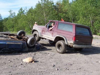 1996 Ford Bronco - An off-road SUV maneuvers around a vehicle that has overturned on a dirt track.