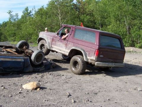 1996 Ford Bronco - A maroon Ford Bronco navigates a dirt path next to a flipped-over car.