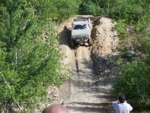 1996 Ford Bronco - A tan SUV navigates a challenging dirt incline surrounded by lush green foliage.