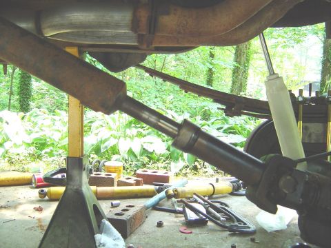 1986 Ford Bronco - Underside view of a vehicle chassis showing a driveshaft, rusty exhaust pipe, and leaf spring suspension, with the vehicle raised on a jack…