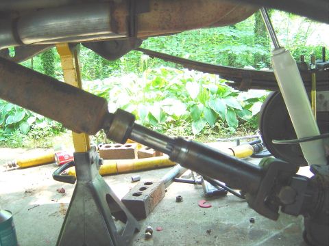 1986 Ford Bronco - Underside view of a vehicle showing the driveshaft with slip yoke separated, a leaf spring, a white shock absorber, and a rusty frame rail,…