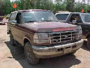 1996 Ford Bronco - A maroon Ford Bronco is parked outdoors next to another vehicle.