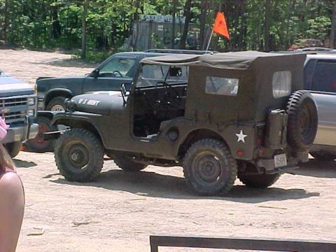 1996 Ford Bronco - A military jeep with a soft top is parked next to other vehicles in an outdoor setting.