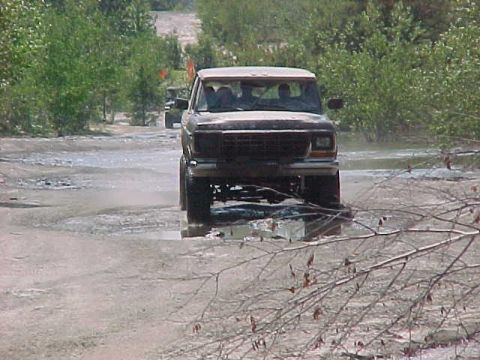 1996 Ford Bronco - A 1996 Ford Bronco navigates through a muddy, water-filled terrain, with another vehicle visible in the background.