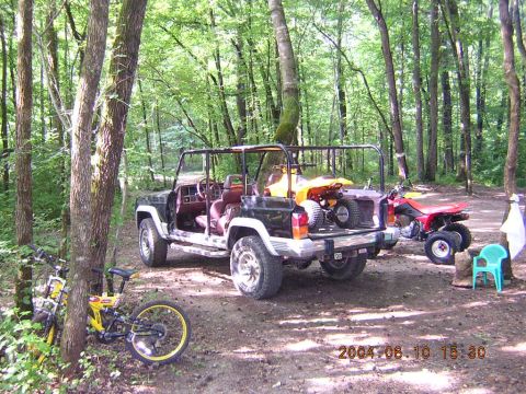 1984 Chevrolet Blazer - A Jeep Cherokee and ATVs are parked in a wooded area, with a bicycle nearby.