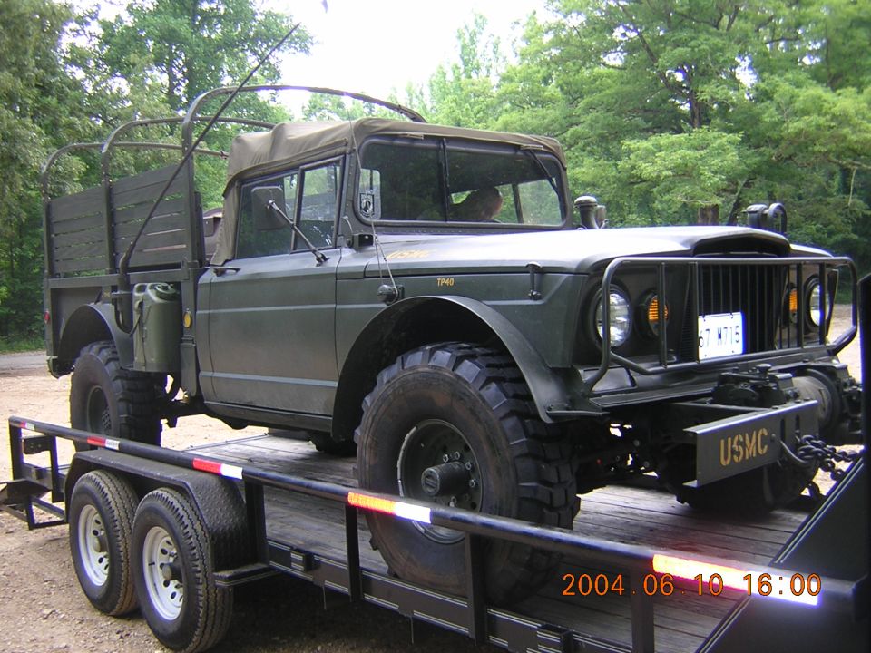 Olive-drab Kaiser Jeep M715 military pickup with USMC bumper markings on a flatbed trailer