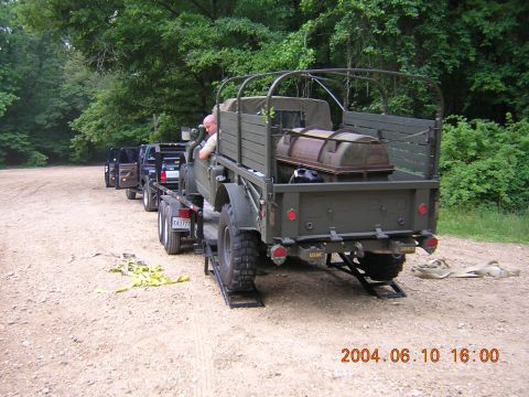 1984 Chevrolet Blazer - Military truck towing a pickup truck on a dirt road with trees in the background.
