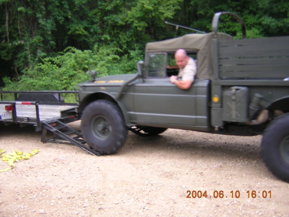 Olive drab military 4x4 cargo truck driving off a flatbed trailer on gravel
