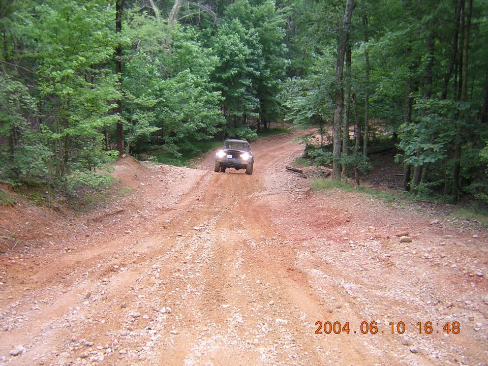Off-road vehicle driving up a rocky dirt path in a forest