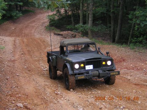 1984 Chevrolet Blazer - A military-style Jeep M715 navigates a wooded dirt road, showing off its off-road capabilities.