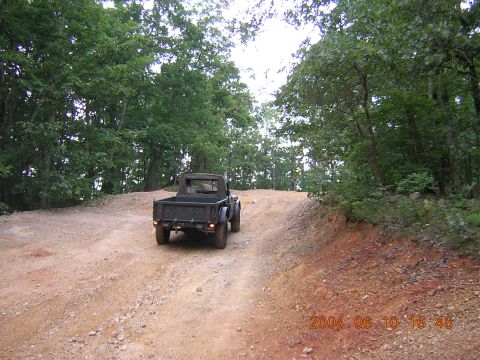 1984 Chevrolet Blazer - A dark pickup truck drives up a dirt road surrounded by trees.