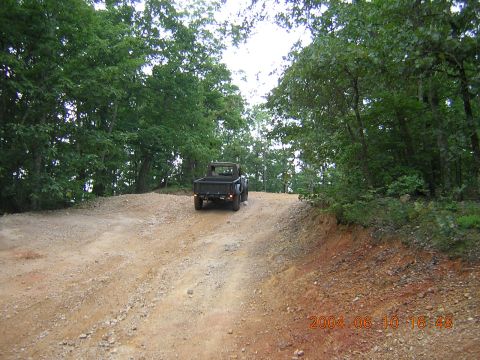 1984 Chevrolet Blazer - A black pickup truck navigates a dirt road through a wooded area.