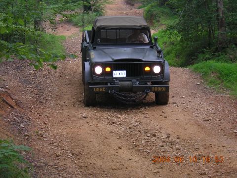 1984 Chevrolet Blazer - A military truck with "USMC" and "309131" visible drives on a gravel road through trees.