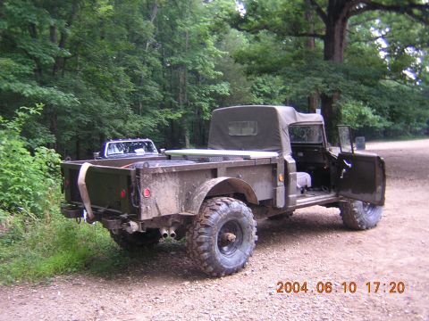 1984 Chevrolet Blazer - This military truck is parked on a dirt road, with trees in the background and another vehicle behind it.