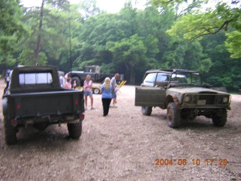 1984 Chevrolet Blazer - Two military-style trucks are parked outdoors on a gravelly surface with trees in the background.