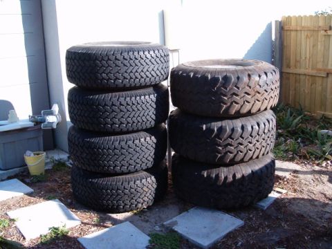 1991 Ford Bronco - A collection of tires are stacked in an outdoor area, with a fence and building visible in the background.