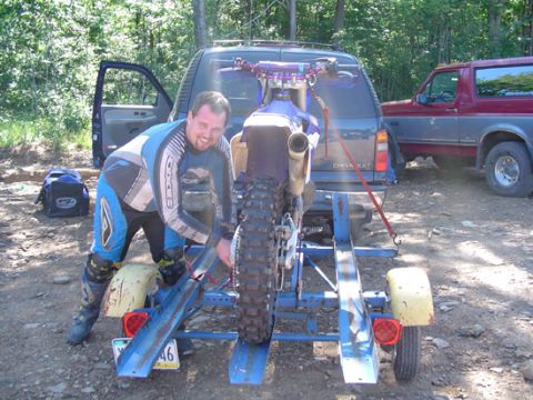 1979 Ford Bronco - A man prepares a dirt bike for transport, with two vehicles visible in the background.