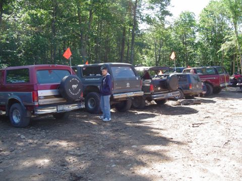 1979 Ford Bronco - Several Ford Broncos are parked in a line on a dirt lot, with trees in the background.