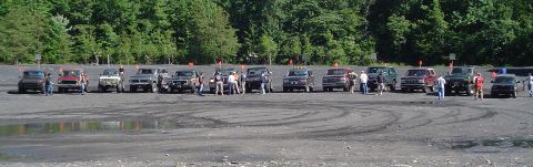 1979 Ford Bronco - Several off-road vehicles are lined up in a dirt area with trees in the background.