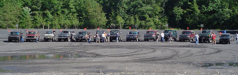 Multiple SUVs and trucks parked in a dirt lot with tire tracks