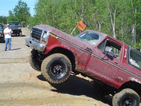 1979 Ford Bronco - A red Ford Bronco navigates an off-road trail, kicking up dirt as it climbs.