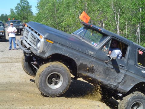 1979 Ford Bronco - A dark-colored SUV with lifted suspension and large tires navigates a dirt track, kicking up mud.