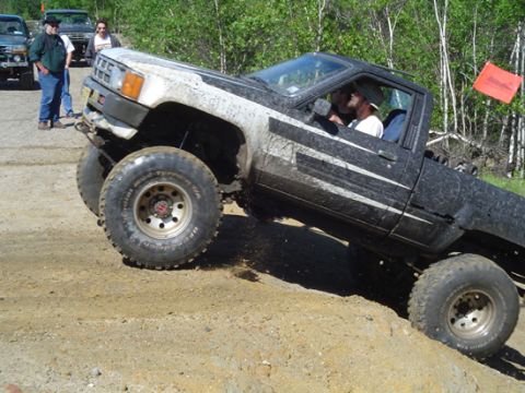 1979 Ford Bronco - Pickup truck with lifted suspension and oversized tires navigates a steep dirt incline during an off-road event.