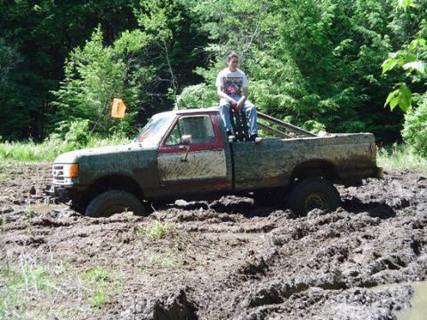 1979 Ford Bronco - A mud-splattered pickup truck is stuck deep in a muddy terrain, with a person sitting on the tailgate.
