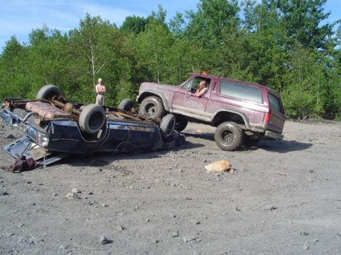 1979 Ford Bronco - Two vehicles are wrecked on a dirt road with trees in the background.