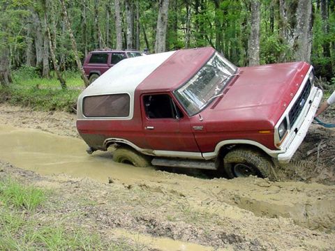 1979 Ford Bronco - A red and white SUV is stuck in the mud with a second SUV visible behind it in the woods.