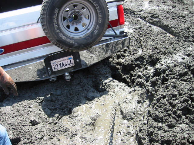 Rear of a white Ford Bronco buried in deep mud with rear spare and CA plate