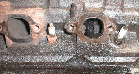 1990 Ford Bronco - Close-up of an engine block showing spark plug holes and exhaust ports, one of which is heavily carbonized.