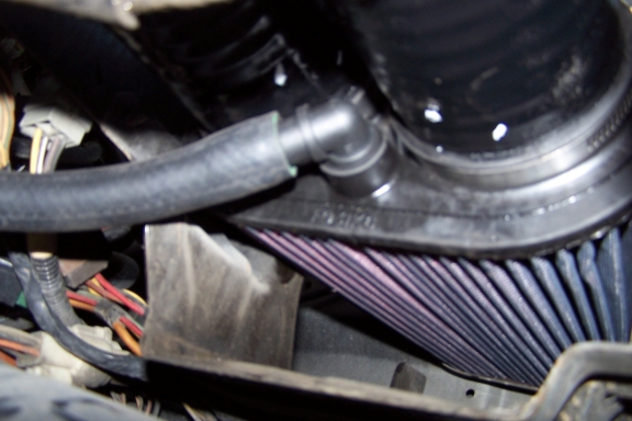 Red K&N pleated air filter in engine bay below black intake tube and breather hose
