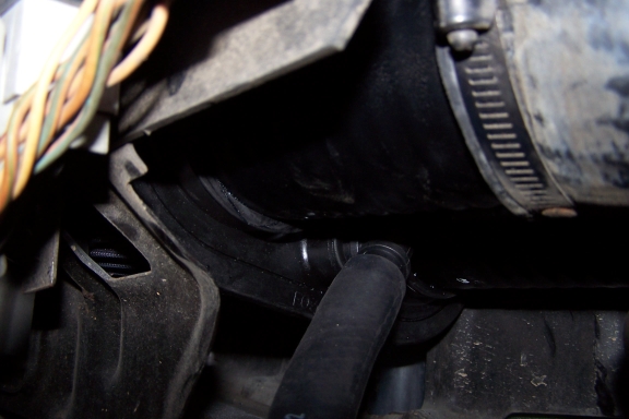 Dark engine bay close-up of black airbox, clamped intake duct and curved rubber hose