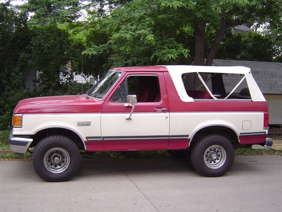 Red and white Ford Bronco with rear top section opened showing red interior in a driveway