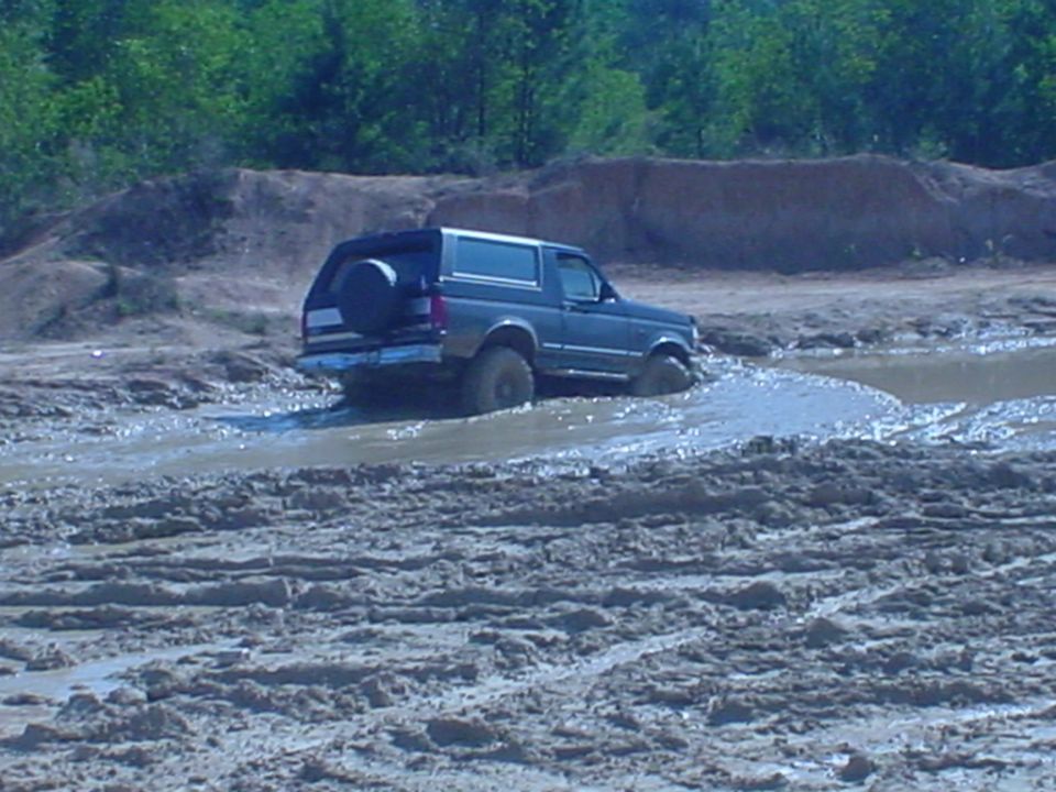 Dark gray Ford Bronco with rear spare carrier driving through a muddy off-road pit