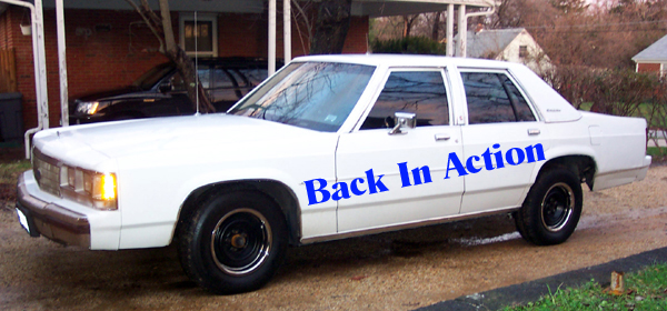 White Ford Crown Victoria sedan with A-pillar spotlight and blue Back In Action text overlay