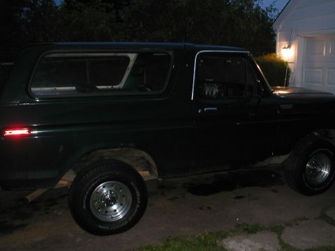 1979 Ford Bronco - Side profile of a dark green 1979 Ford Bronco parked in front of a garage.