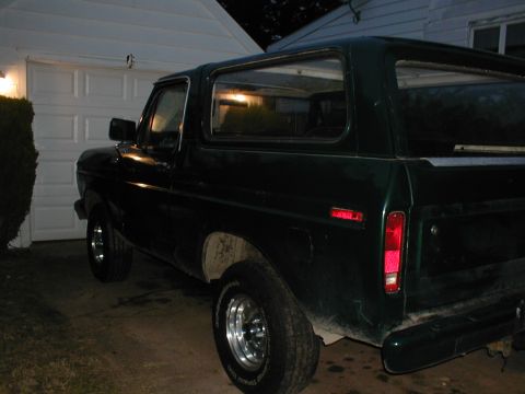 1979 Ford Bronco - Rear quarter view of a dark green Ford Bronco parked in front of a garage.