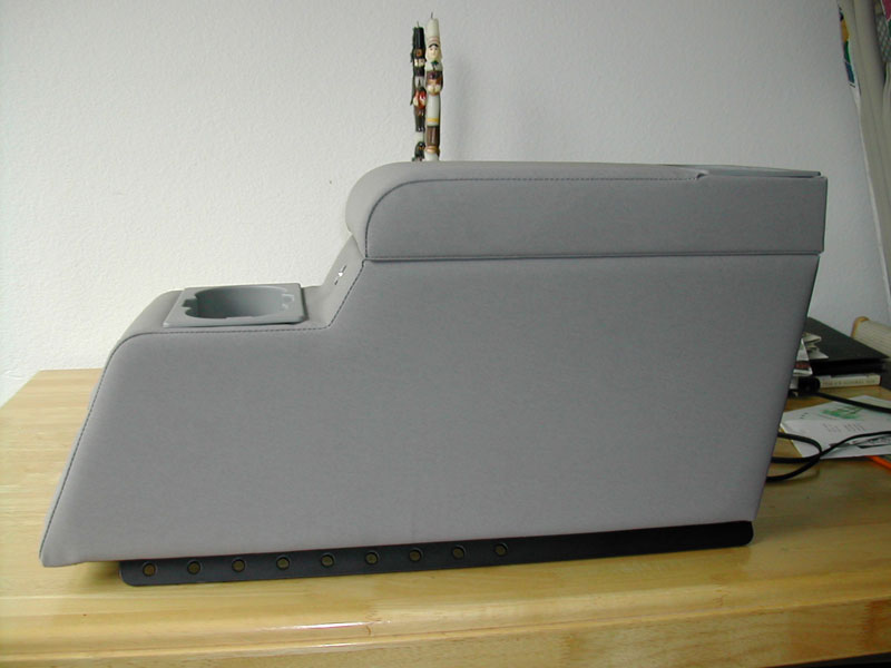 Gray center console with a cup holder and a padded armrest, viewed from the side