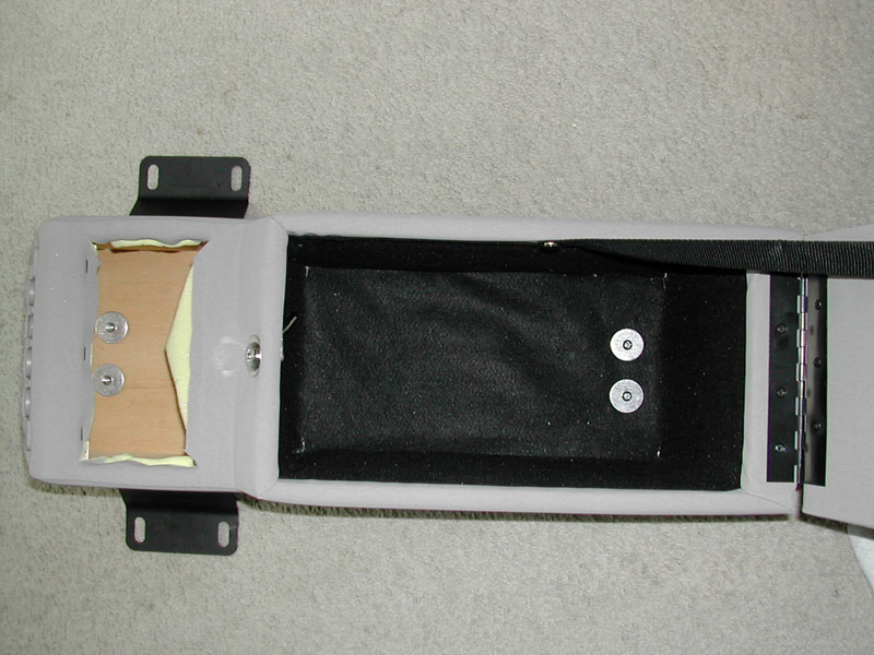 Open gray center console armrest with black felt-lined storage bin and mounting brackets, laid on carpet