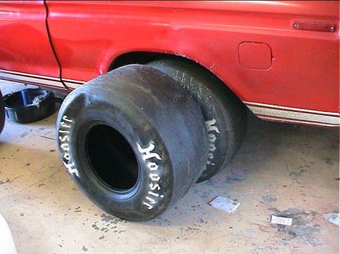 1979 Ford Bronco - Two large Hoosier racing tires are shown next to a red vehicle, possibly being prepared for a race.