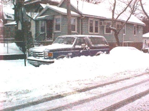 1989 Ford Bronco - This blue SUV is mostly buried in snow, with only its front grille and part of the hood visible.