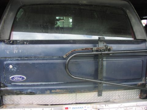 1988 Ford Bronco - Rear view of a dark blue Ford Bronco with a spare tire mount and diamond plate bumper.