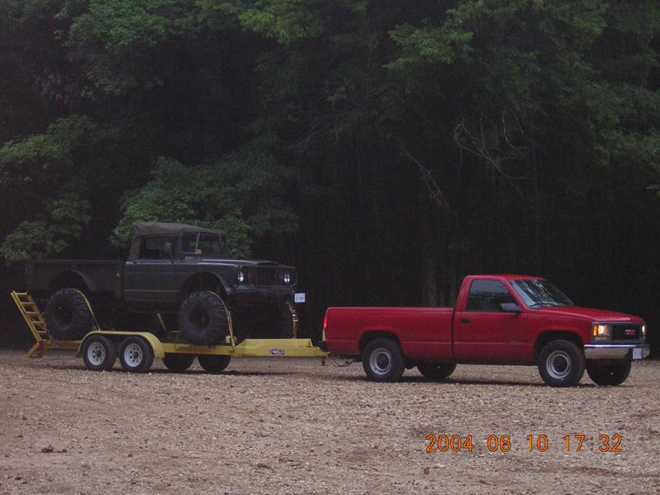 Dark off-road truck on yellow trailer towed by red GMC pickup, side view